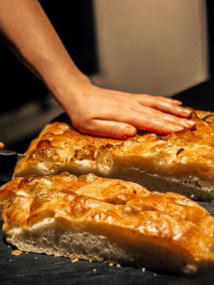 Close-up of hands cutting freshly baked focaccia bread on a dark surface.